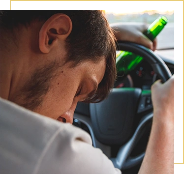 Drunk young man driving a car with a bottle of beer